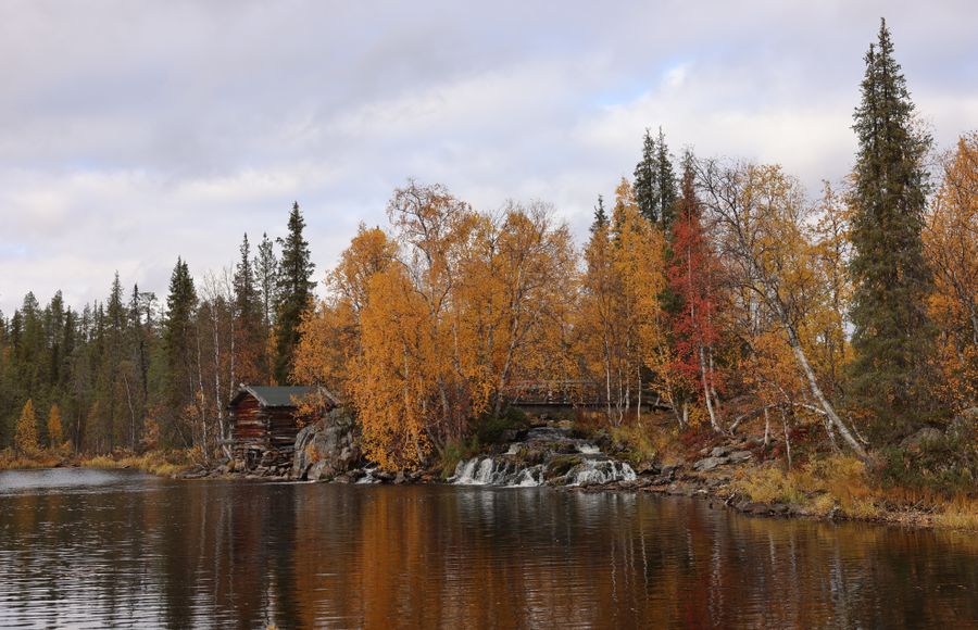 Mökki joen rannalla syksyn väreissä